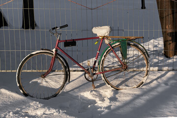 Bicycle standing in the snow at the fence