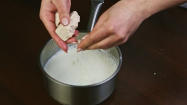 slow motion closeup female hands crush up dry yeast into hot milk in metal saucepan