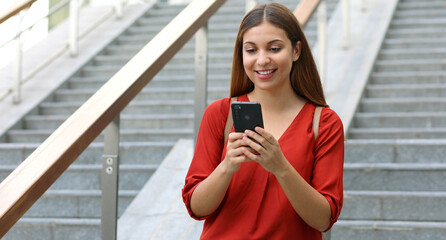 Portrait of beautiful woman walking down the stairs holding her phone