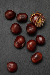Fresh chestnuts and a chestnut hedgehog on dark grey slate table. Raw Chestnuts for Christmas. Flat lay