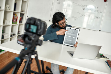 Javascript online. Young man teaching explaining java basics while working online from home. Recording video tutorial. Focus on a teacher