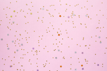 Golden stars shaped confetti glitter on pink background.