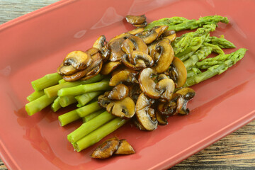 Cooked fresh asparagus with mushroom sauce on red serving plate