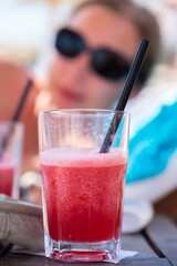 Cocktail on the table. Glass of juice on the table against the blurred silhouette of a woman's face in sunglasses. Selective focus