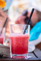 Cocktail on the beach. Glass of juice on the table against the blurred silhouette of a woman's face in sunglasses. Selective focus