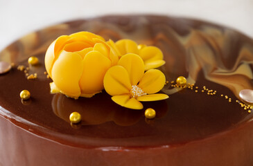 Chocolate cake with yellow flower. Chocolate cake with flower. Chocolate mousse cake in mirror glaze. Cake decor details. Shallow depth of field