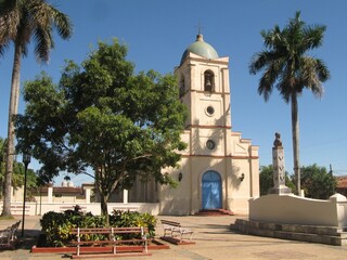 Main square in Viñales with small cream-colored church surrounded by palm trees, Cuba