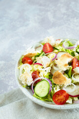 Traditional Middle Eastern salad fattoush with toasted pita bread and vegetables in the white plate on the napkin. Healthy vegetarian food. Close up, copy space, light background.