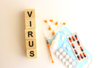 The words VIRUS is made of wooden cubes on a white background with medical drugs and medical mask. Medical concept.
