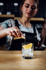 Girl bartender adds syrup to a glass with ice and lemon while making a cocktail - female drink