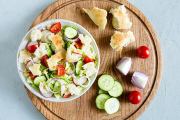 Delicious fattoush salad with bread pita, fresh vegetables and basil on plate on the wooden stand. Traditional middle eastern or arabic food. Close up, flat lay, light background.