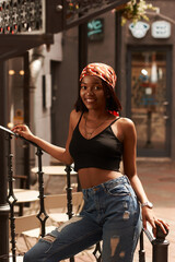 Young beautiful stylish african woman standing and posing. Girl in jeans and black shirt. Outdoor summer fashion lifestyle portrait.