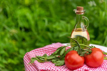 Olive oil in bottles with tomatoes and herbs on a green background with space to copy.