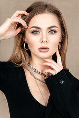 Portrait of a beautiful girl with blue eyes close-up, looking at the camera, hands at her face. Metal accessories.Black clothes.Beige background.