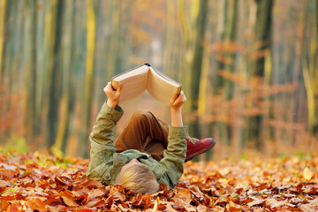 Child reading a book, colorful autumn in the park. Hobbies and rest.