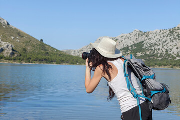 Wanderlust of a young woman, photographer and traveler. The woman is walking on the mountains and roads of the island of Majorca, the girl is wearing a hat and is taking photos. The woman is happy