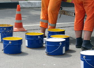 Repair work on the road. Workers in orange uniforms paint yellow and white on the pedestrian crossing.