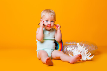 Toddler girl in blue bodysuit, sunglasses, swimming circle sits on a yellow background. concept of summer holidays with children, space for text