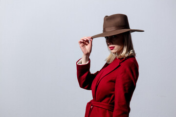 Blonde girl in red coat and vintage hat on grey background