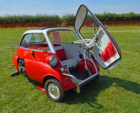 Classic red and white  BMW Isetta 300,  3 wheeled bubble car parked on grass.