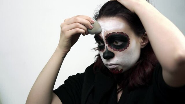 Girl doing makeup skeleton for the feast of Santa Muerte. Theme of costumes and transformation for holiday of Halloween. Traditional skull makeup for the day of the dead celebration