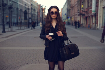 Obraz premium Young beautiful pretty girl walking along the street with handbag and cup of coffee.