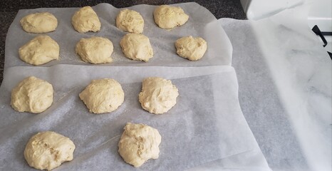 Homemade dough balled for English Muffins rising on parchment paper on a kitchen counter.