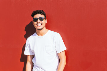 portrait of a young man with sunglasses smiling on a red wall