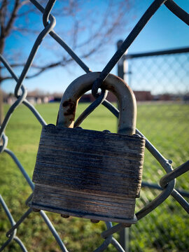 A closeup old rusty gray padlock on a school's chain link fence.