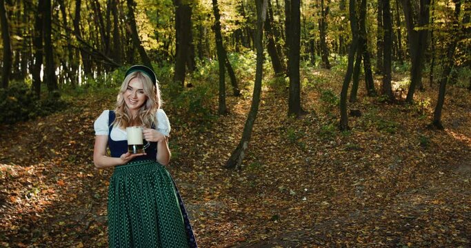 Happy Slavic girl in national costume poses with a mug of beer in autumn forest