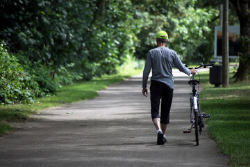 Portrait on back vieww of man walking in urban park pushing his bicycle