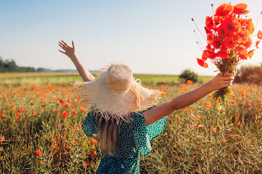 Young woman raised arms holding bouquet of poppies flowers walking in summer field. Happy girl feeling free