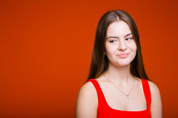 Emotional portrait of a European girl with long hair who playfully looks away on an orange background