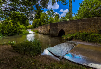 Fototapeta na wymiar A panorama view of the bridge and ford over the River Ise in the town of Geddington, UK in summer