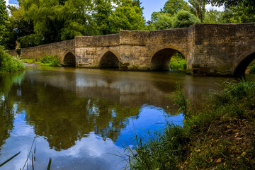 Fototapeta na wymiar A panorama view down the River Ise towards the bridge and ford in the town of Geddington, UK in summer