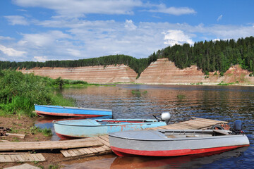 Naklejka na ściany i meble three boats are moored on the river Bank.High Bank, rocky, steep. Exposed geological rock, which is more than 200 million years old. Quiet, Calm. Tourist area. Summer.The photo is horizontal.