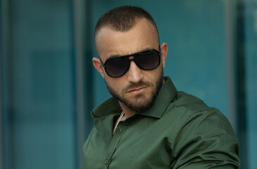 Obraz premium Close up shot of young man. Confident bearded serious handsome man wearing shirt and in sunglasses. Men's beauty, fashion. Outdoor portrait.