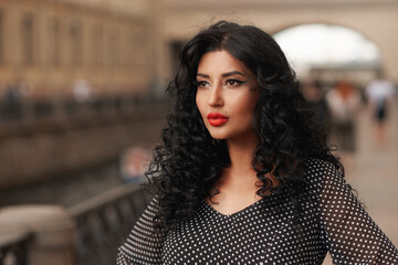 Outdoor closeup face portrait of young brunette woman with afro curly hair, makeup and red lips. Fashion style shot. Elegant girl in black and white polka dot dress