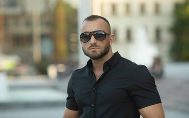 Confident handsome man in sunglasses and shirt over city background. Men's beauty, fashion. Outdoor portrait.