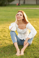 Fototapeta premium Young pretty woman natural outdoor portrait. Beautiful girl sitting at grass at sunset
