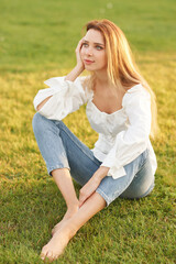 Fototapeta premium Young pretty woman natural outdoor portrait. Beautiful girl sitting at grass at sunset