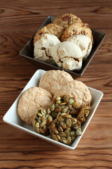 Oatmeal cookies with walnuts and raisins, sugar-coated pumpkin seed cookies,  meringue cookies with hazelnuts, almond cookies in a square bowl on a wooden table. Closeup