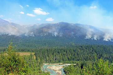 Fototapeta na wymiar Wildfires near Glacier National Park in Canada. The view on the smoke coming out of the woods / forest with hazy sky in the background.