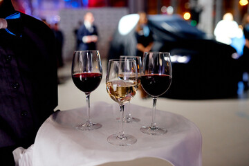waiter with a tray with glasses of red and white wine on a white napkin. The car under the cover is...