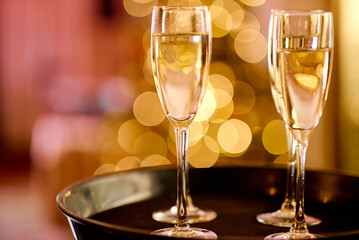 Full glasses of champagne on black tray with colorful bokeh
