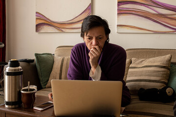 persona trabajando desde su casa en un departamento con sillon cuadros celular computadora y toma mate argentino © patoouupato