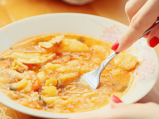 female hand kneads a stew with a fork in a plate on a wooden table,
side view close-up.