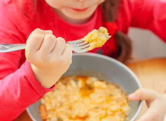 little girl in a red sweater eats stewed potatoes with a fork,
side view close-up.