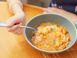 children's hand holds a fork and eats stewed potatoes from a gray plate, closeup side view.