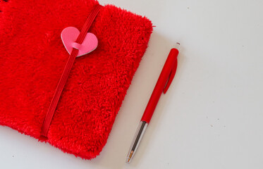 children's notebook of red color from a fur structure with a heart and pen on a white table, close-up top view.